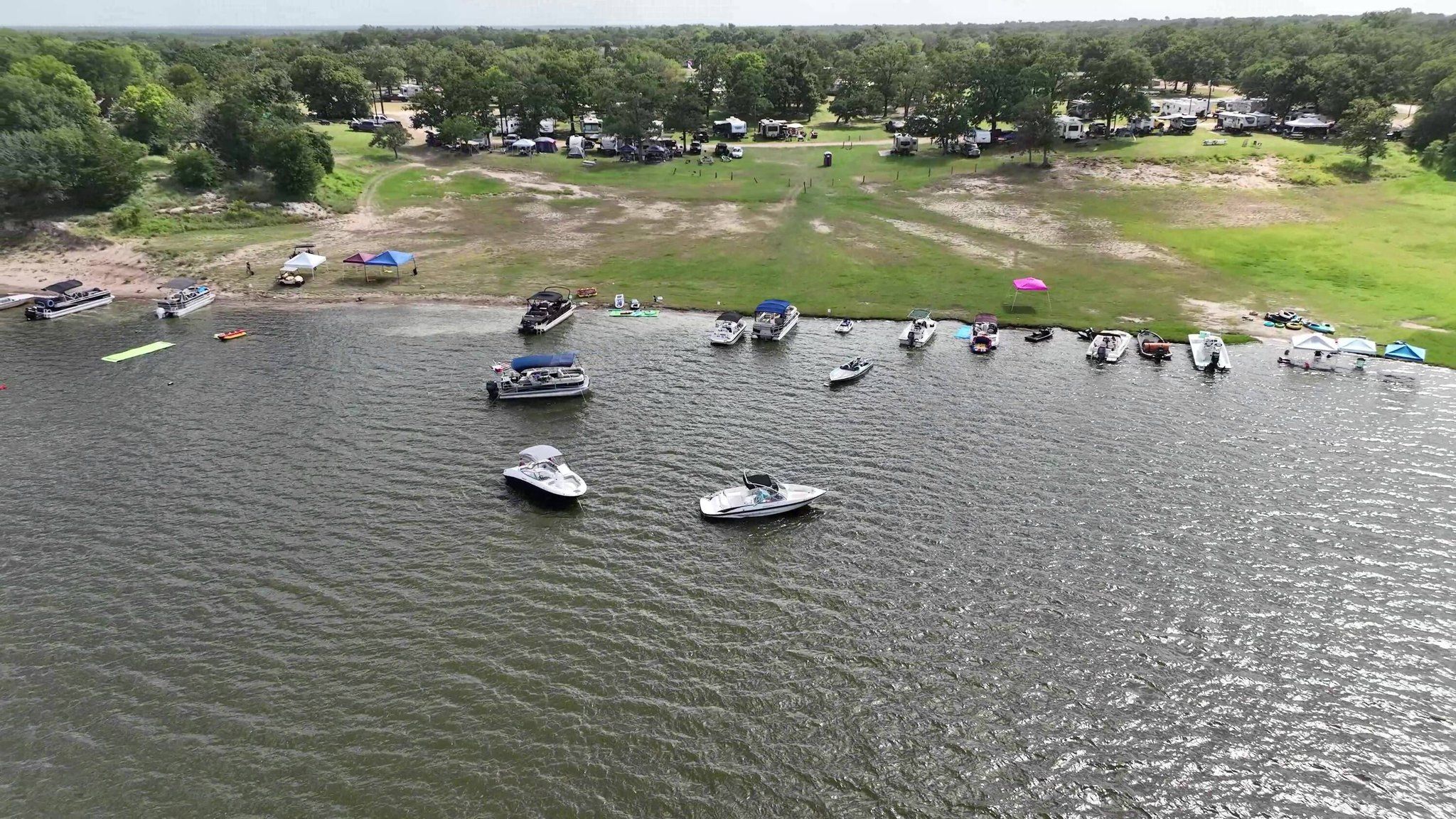 Aerial view of a sandy cove on Lake Somerville with boats along the shoreline and campers spread across the wooded grounds.