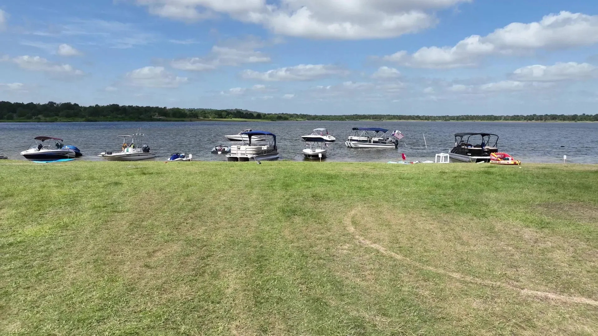 Boats anchored and pulled up along the shoreline of Lake Somerville on a bright day with scattered clouds.