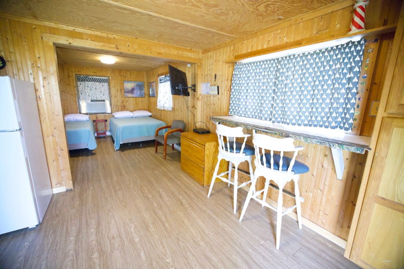 Inside a cabin: living area with bar seating, a refrigerator and beds beyond