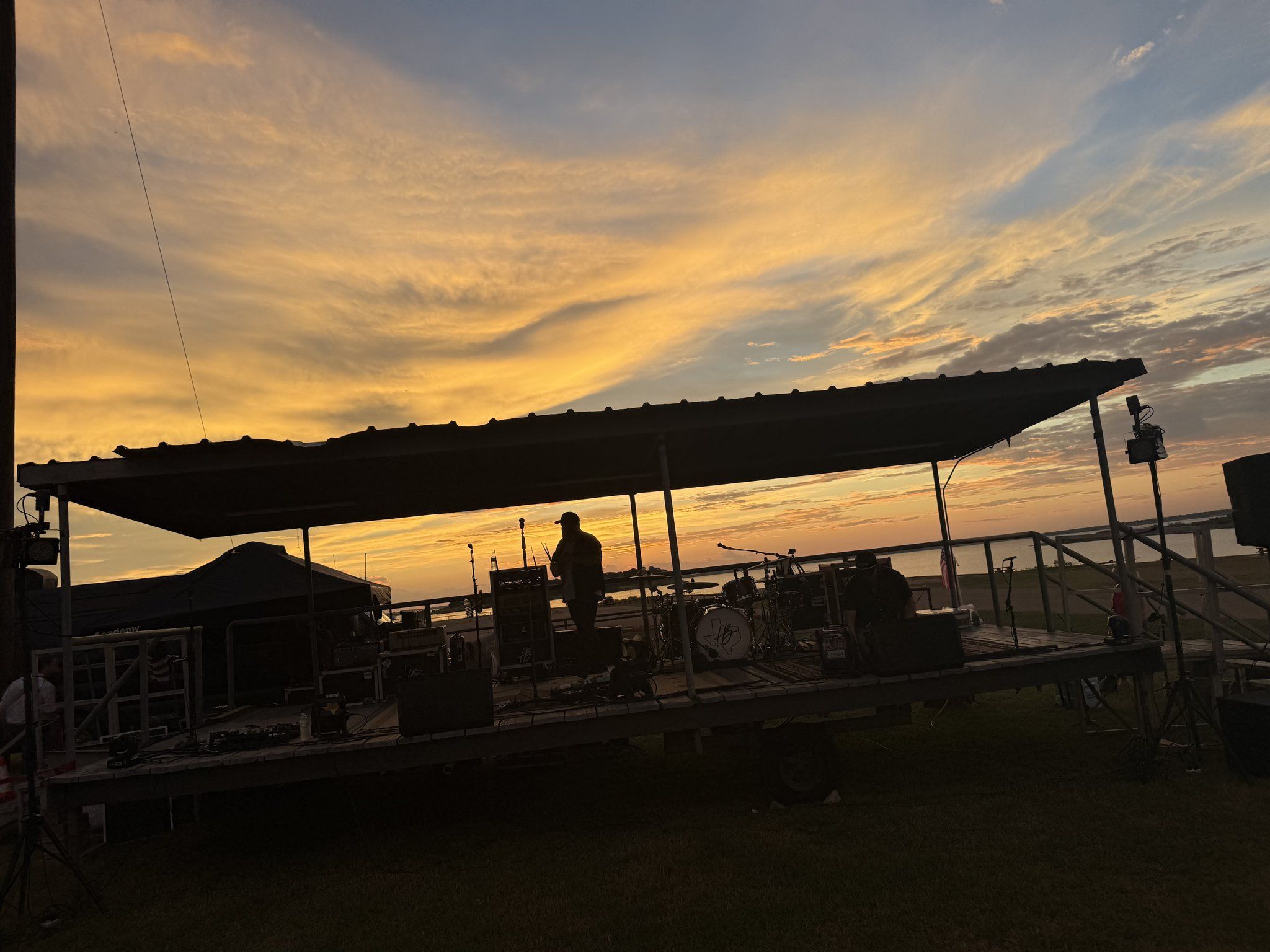 The covered stage at Overlook Park in silhouette against a golden sunset over the lake.
