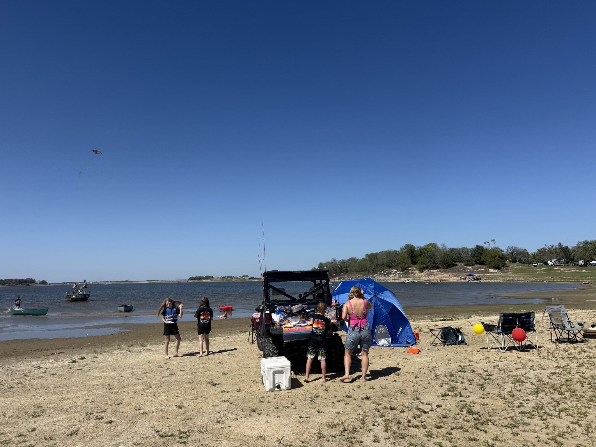 Guests on the sandbar beach with blue umbrellas, camp chairs and coolers, and boats anchored offshore