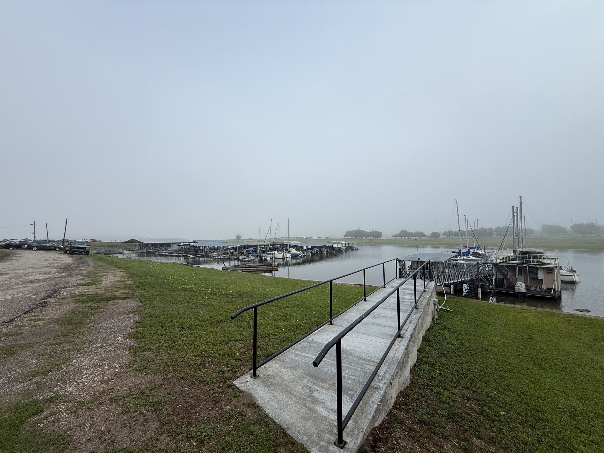 Covered slips and moored boats fading into thick morning fog, seen from the top of the marina access ramp
