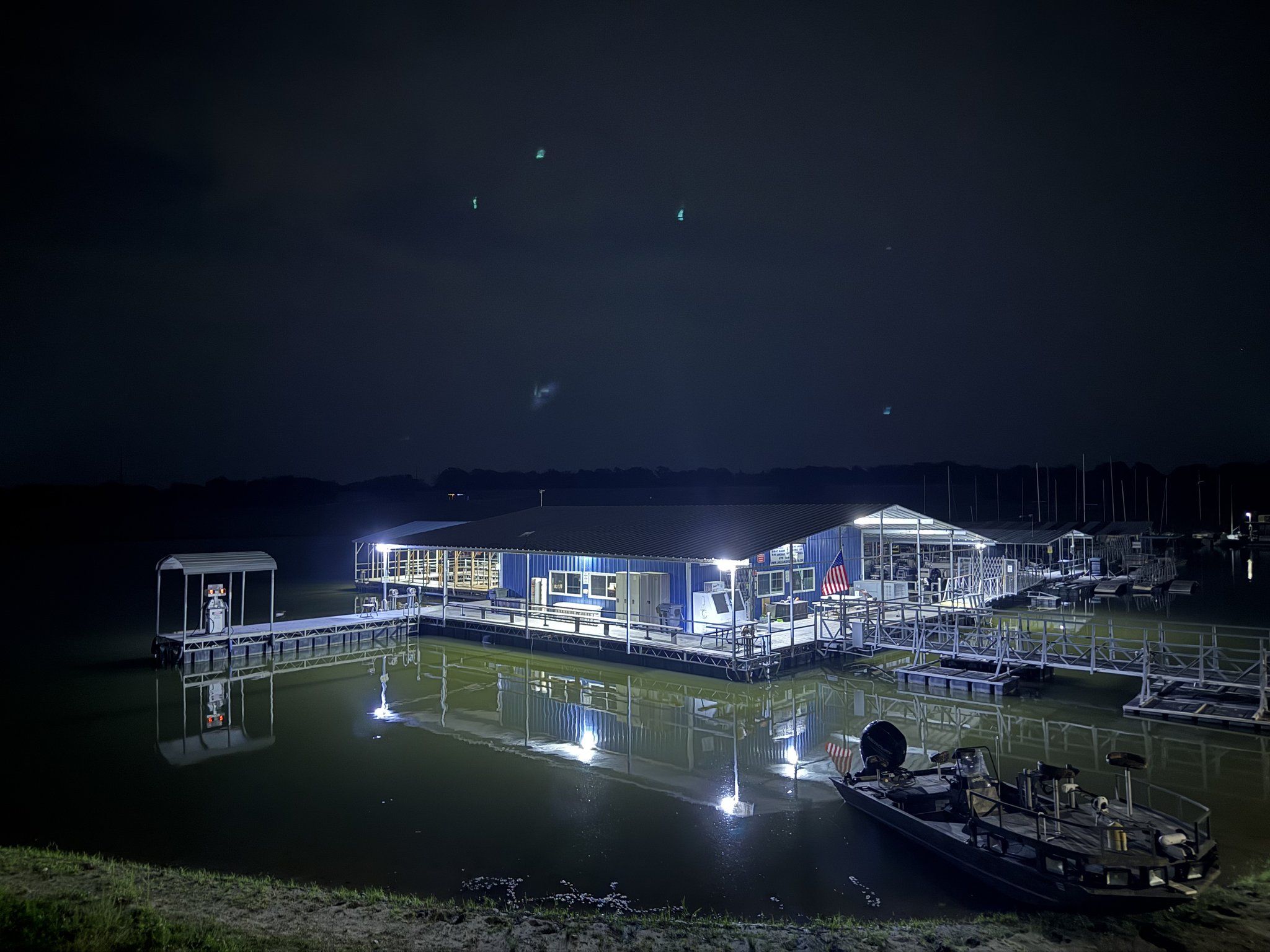 The blue marina building and covered docks floodlit at night and mirrored in black, glassy water.