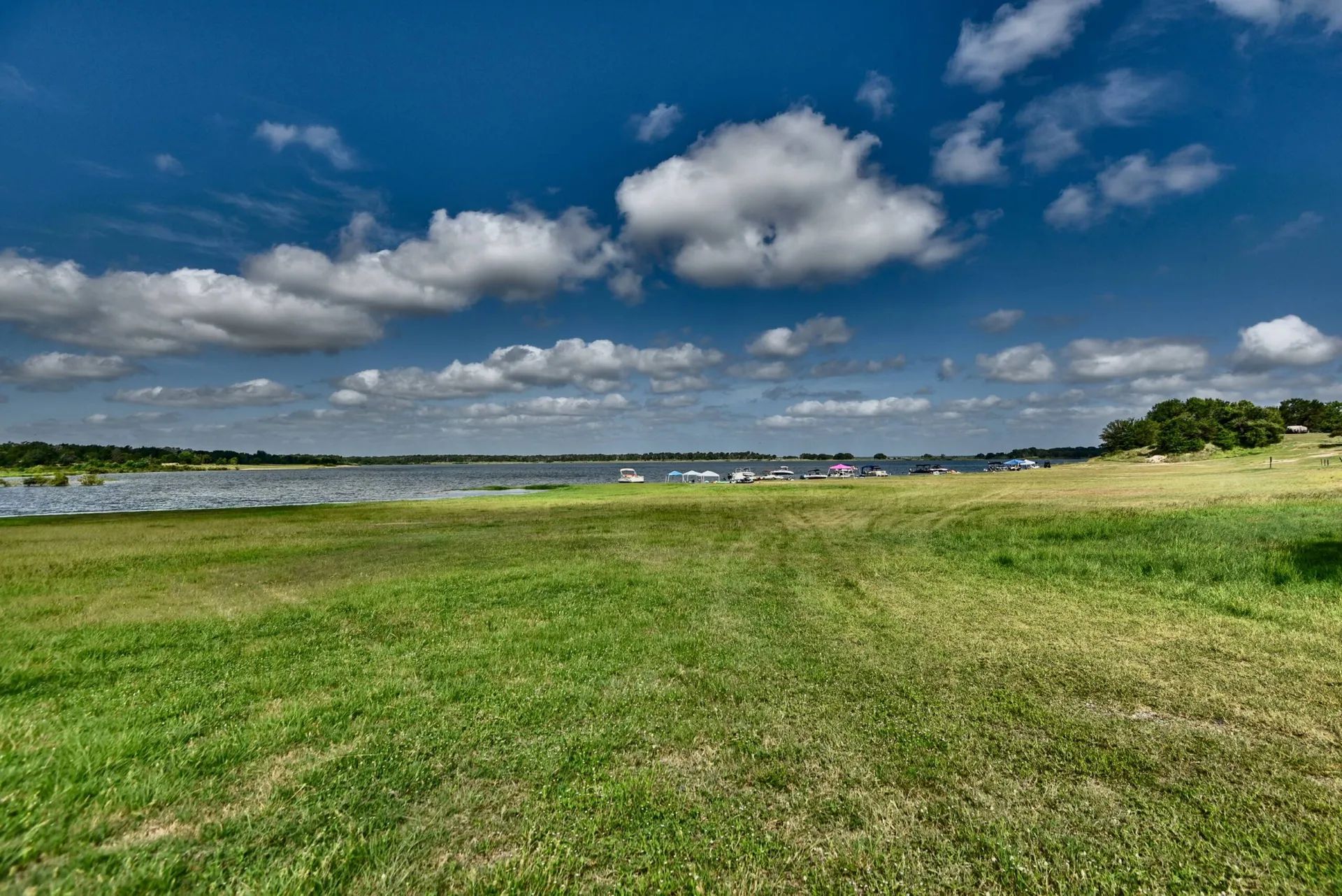 A mown grassy bank leading down to Lake Somerville under a deep blue sky, with a row of boats pulled up along the far shore.