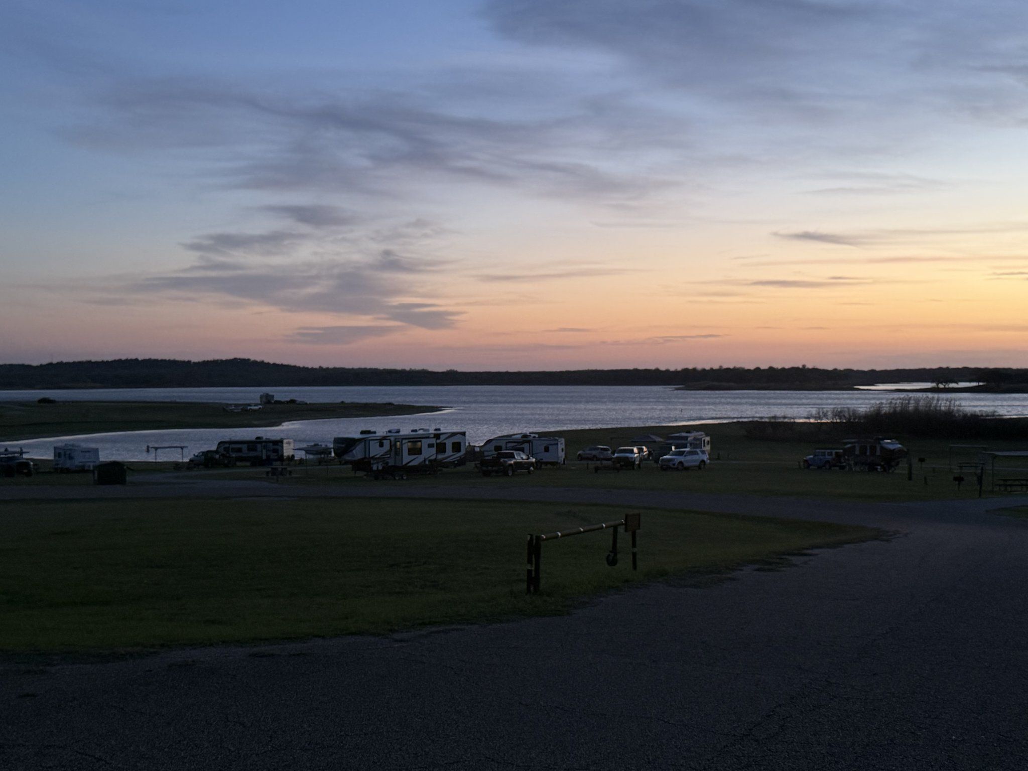Elevated view of travel trailers and motorhomes in the RV park at dusk with Lake Somerville behind