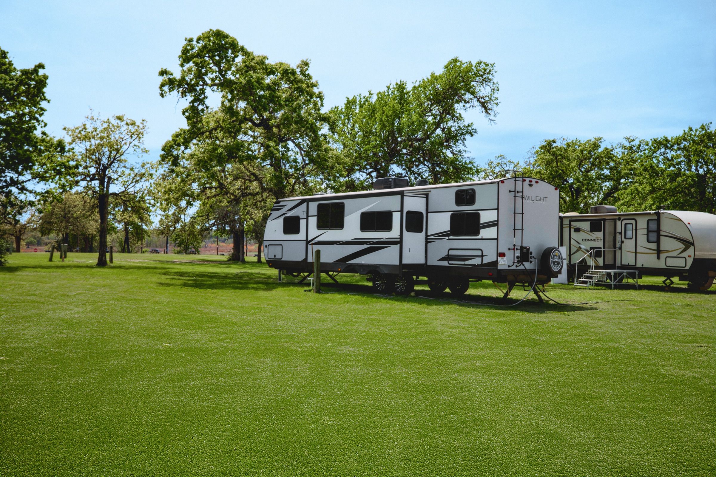 Travel trailers parked on green grass under shade oaks at an RV site at Overlook Park & Marina