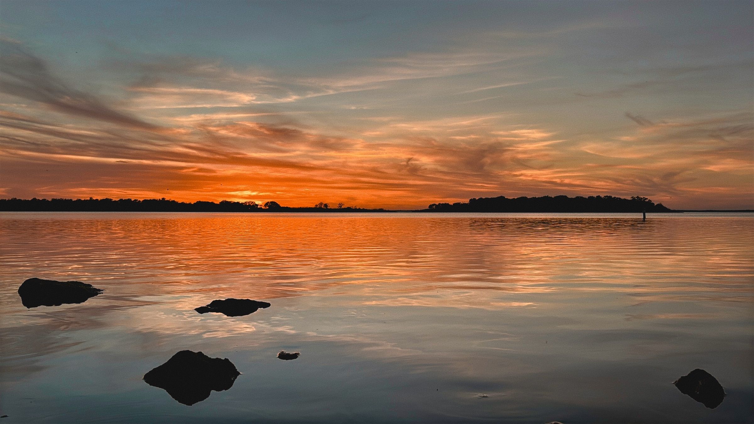 Vivid orange sunset over calm Lake Somerville with rock silhouettes in the water