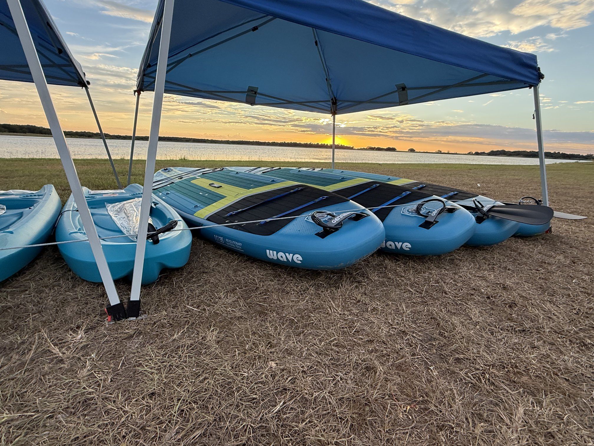 Paddleboards stacked under a canopy at sunset beside the water.
